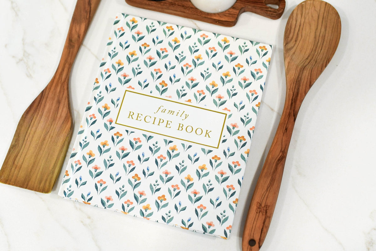Floral-patterned family recipe book with wooden utensils on a white background