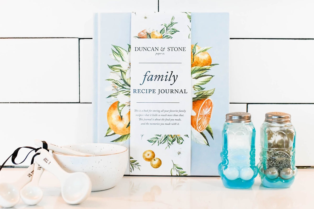 Family Recipe Journal on a kitchen counter with a set of measuring spoons and cups, along with a salt and pepper shaker