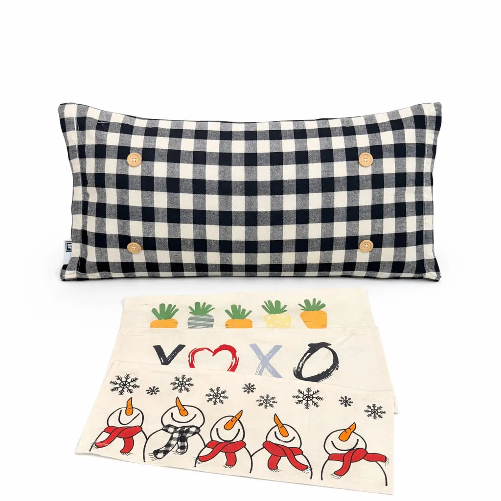 A rectangular throw pillow with a black and off-white buffalo check pattern and four wooden buttons, shown above a matching off-white fabric pouch decorated with snowman illustrations, potted plants, and the letters V, O, X, O.
