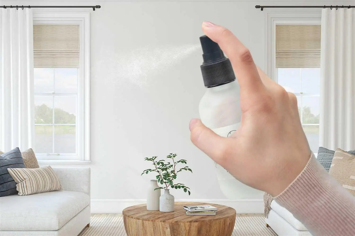 Hand spraying room spray in cozy farmhouse living room with neutral decor and natural light