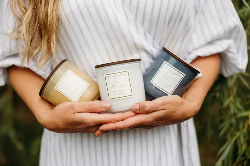Woman holding three farmhouse-style scented candles in cozy cottage decor