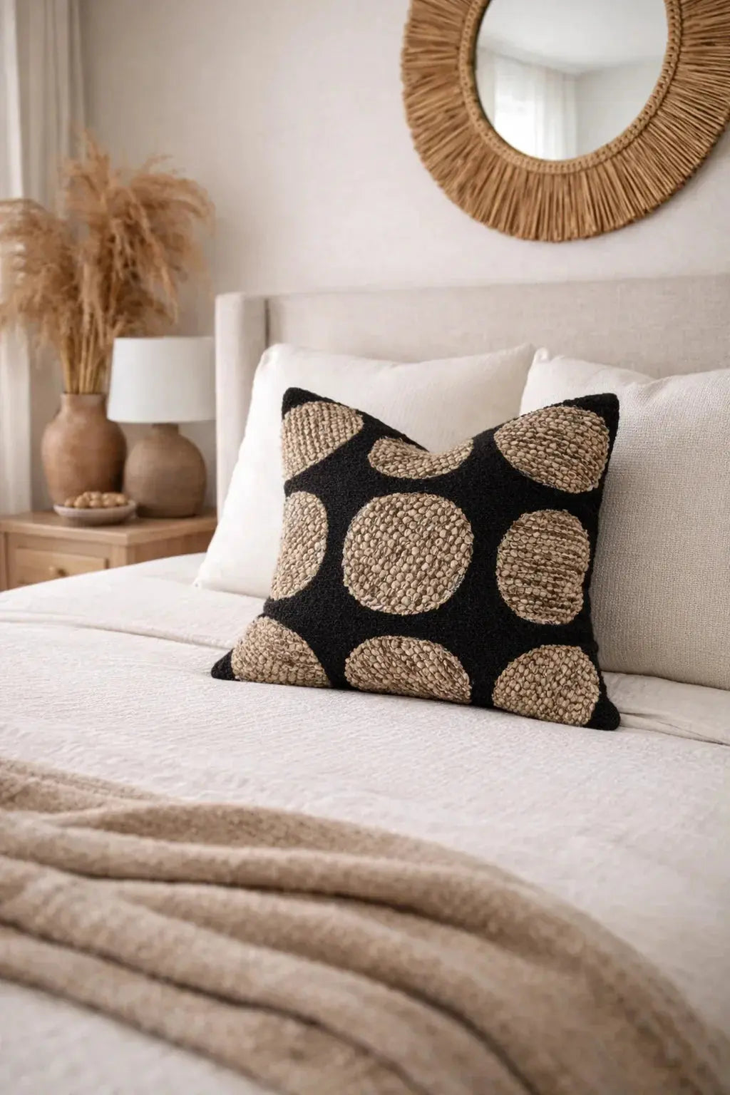 Black and beige textured polka dot throw pillow on cozy farmhouse bed with rattan mirror
