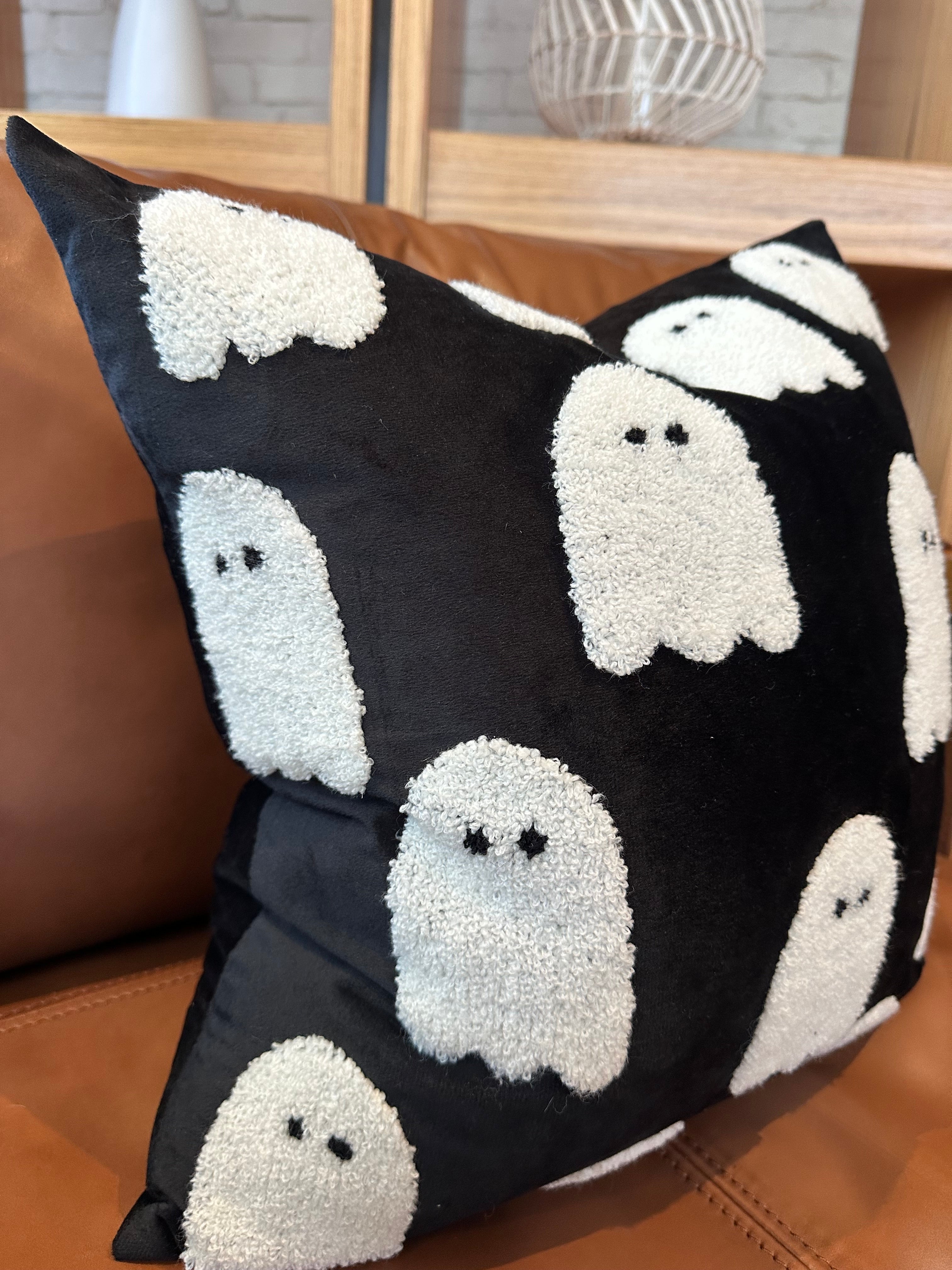 Black pillow with white ghost patterns on a brown couch
