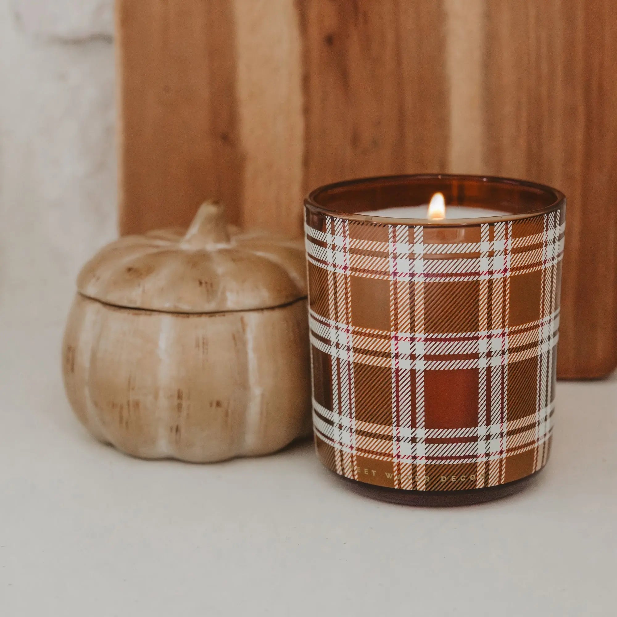 Candle with plaid design next to a pumpkin on a neutral background
