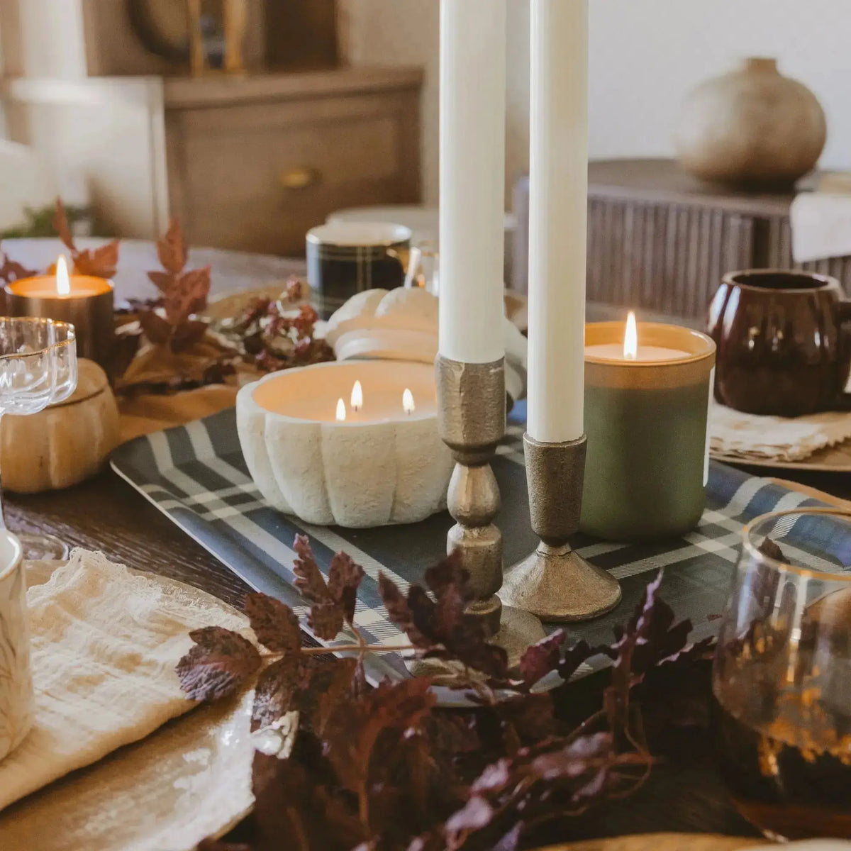 Candlelit table setting with pumpkins and autumn leaves on a wooden table.
