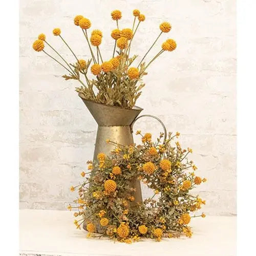 Yellow dried flower arrangement in a rustic galvanized metal pitcher vase, set against a light textured brick wall background.