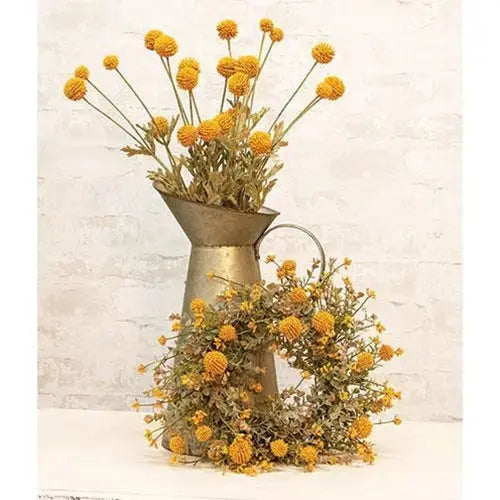 Yellow dried flower arrangement in a rustic galvanized metal pitcher vase, set against a light textured brick wall background.