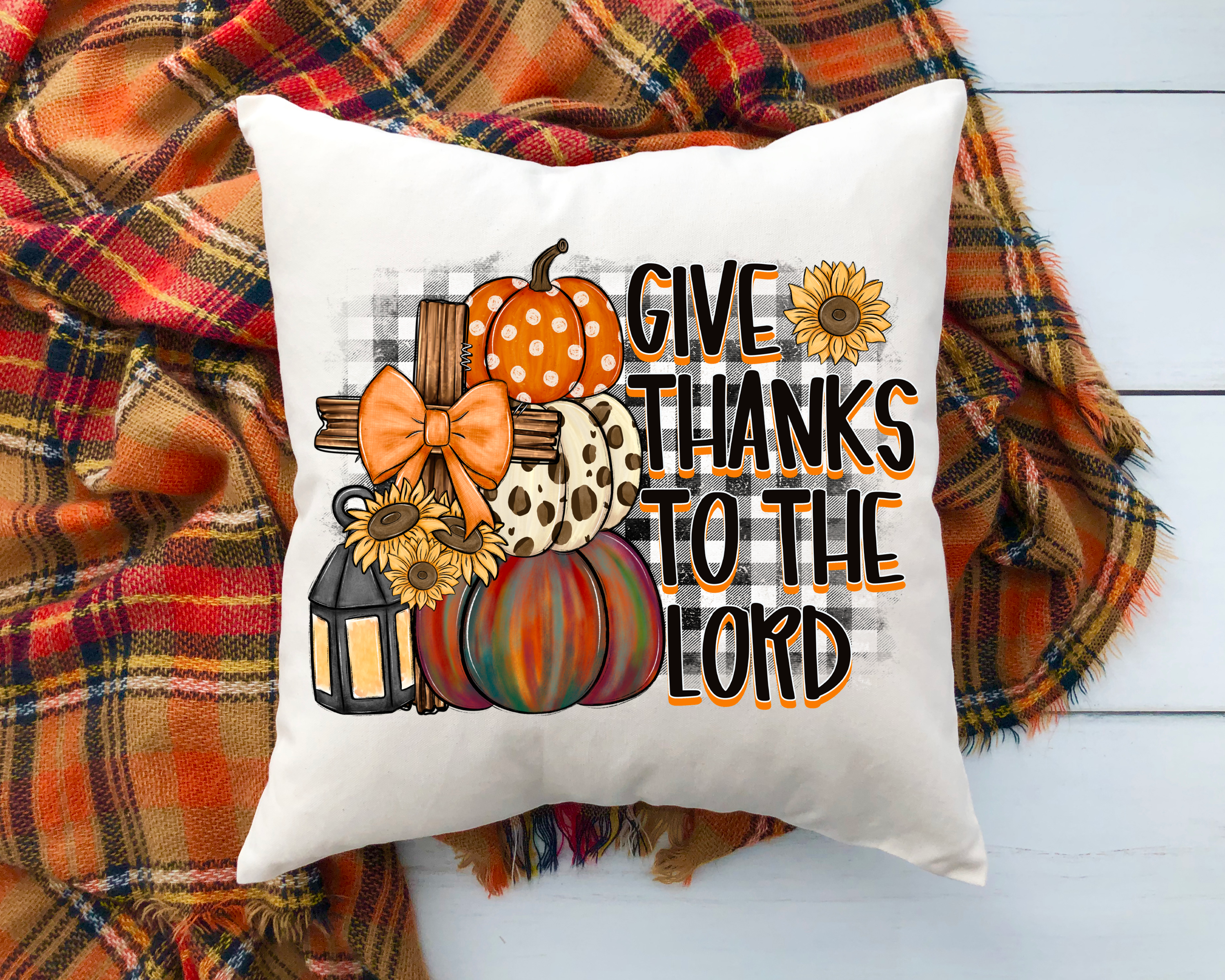 Decorative pillow with autumn-themed design and text 'Give Thanks to the Lord' on a plaid fabric background.