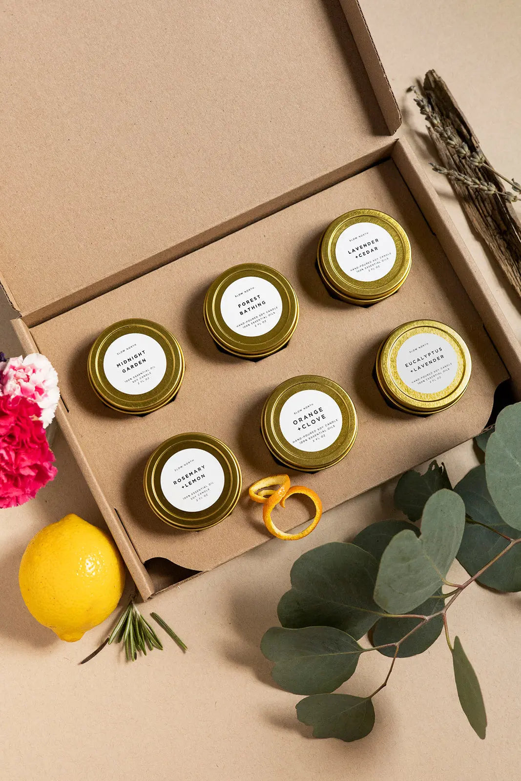 Set of six soy candles in gold tins with natural scents, nestled in a kraft box with lemon, eucalyptus, and dried lavender.