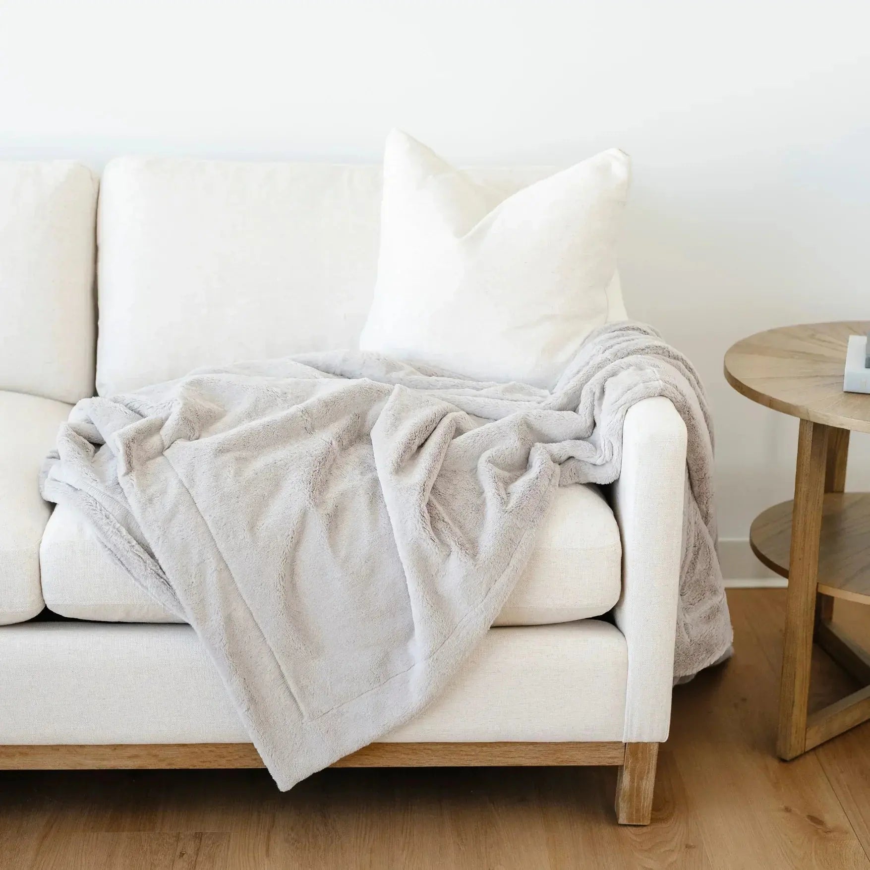 White sofa with a beige blanket and pillows in a minimalistic living room.