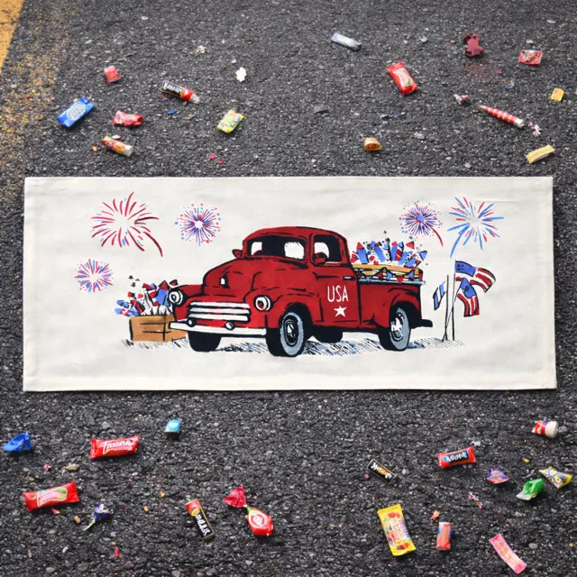 Red truck with patriotic decorations on a white towel, surrounded by scattered candy on a dark surface.