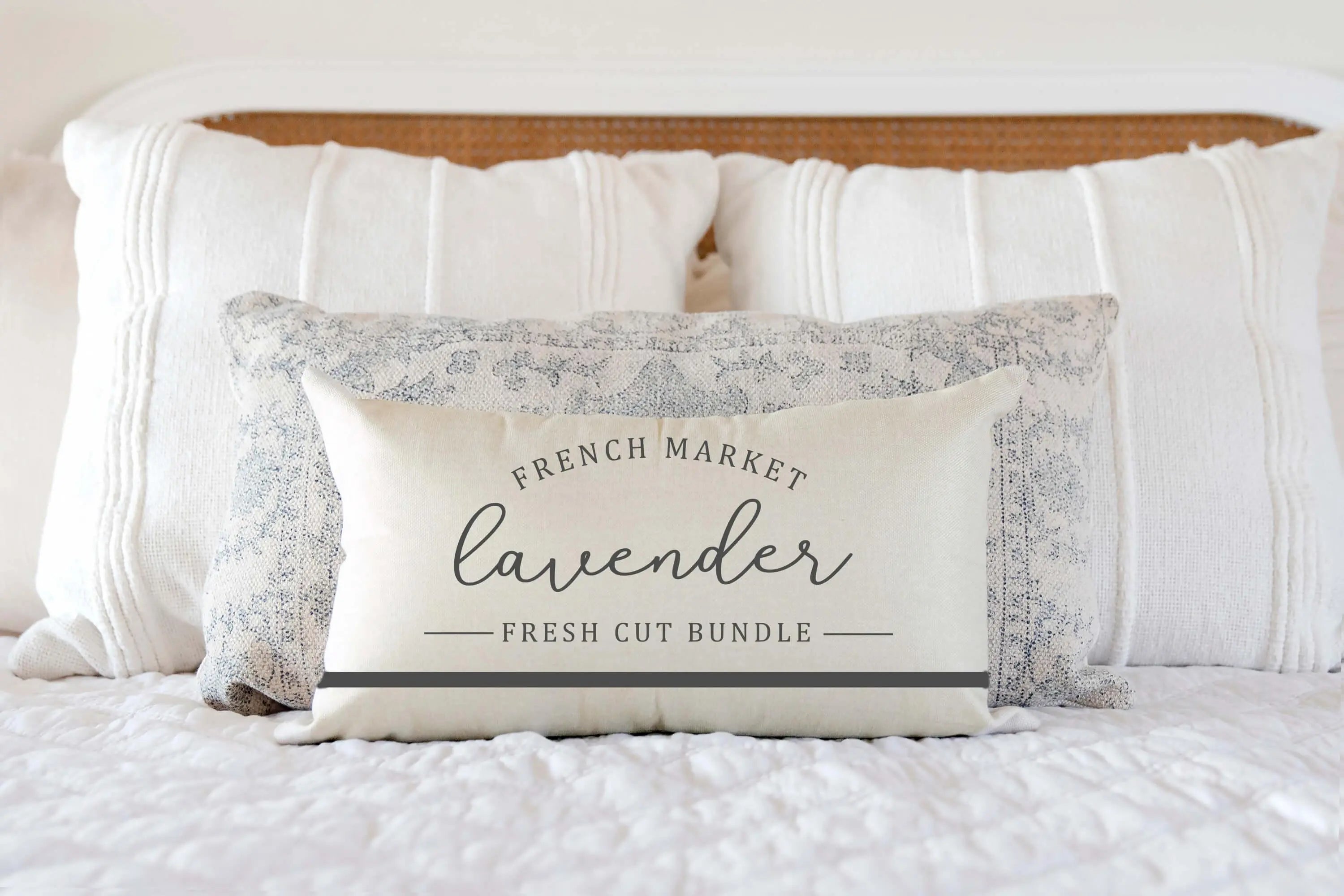 French Market Lavender throw pillow on cozy farmhouse bed with textured white bedding and cane headboard