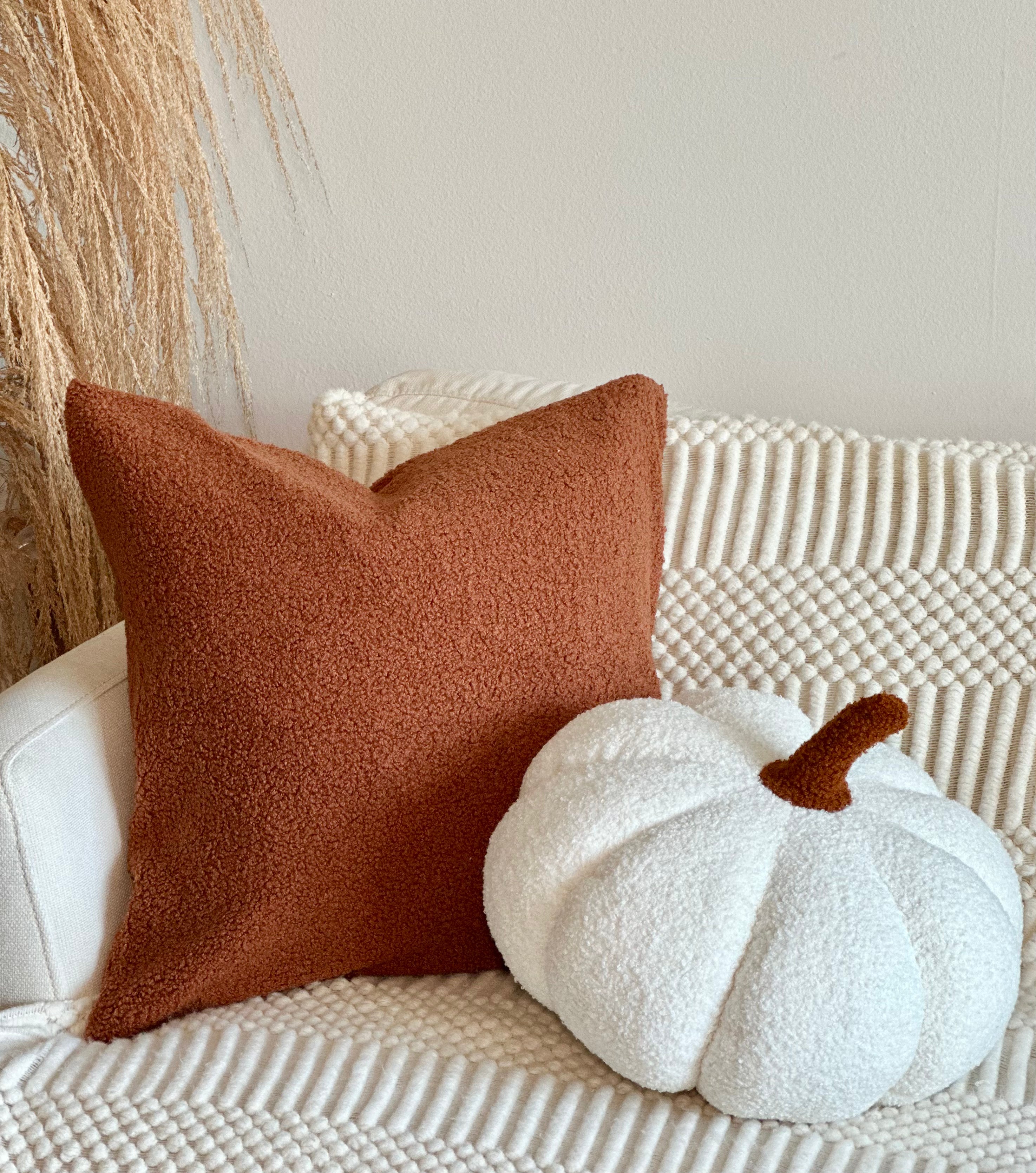 Brown pillow and white pumpkin on a textured surface with a neutral background