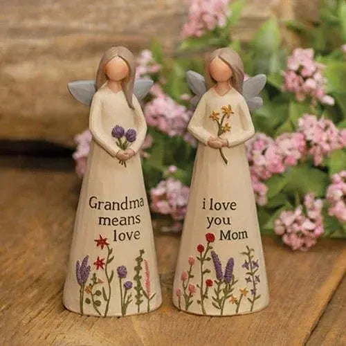 Two angel figurines with floral designs and engraved messages on a wooden surface with flowers in the background.