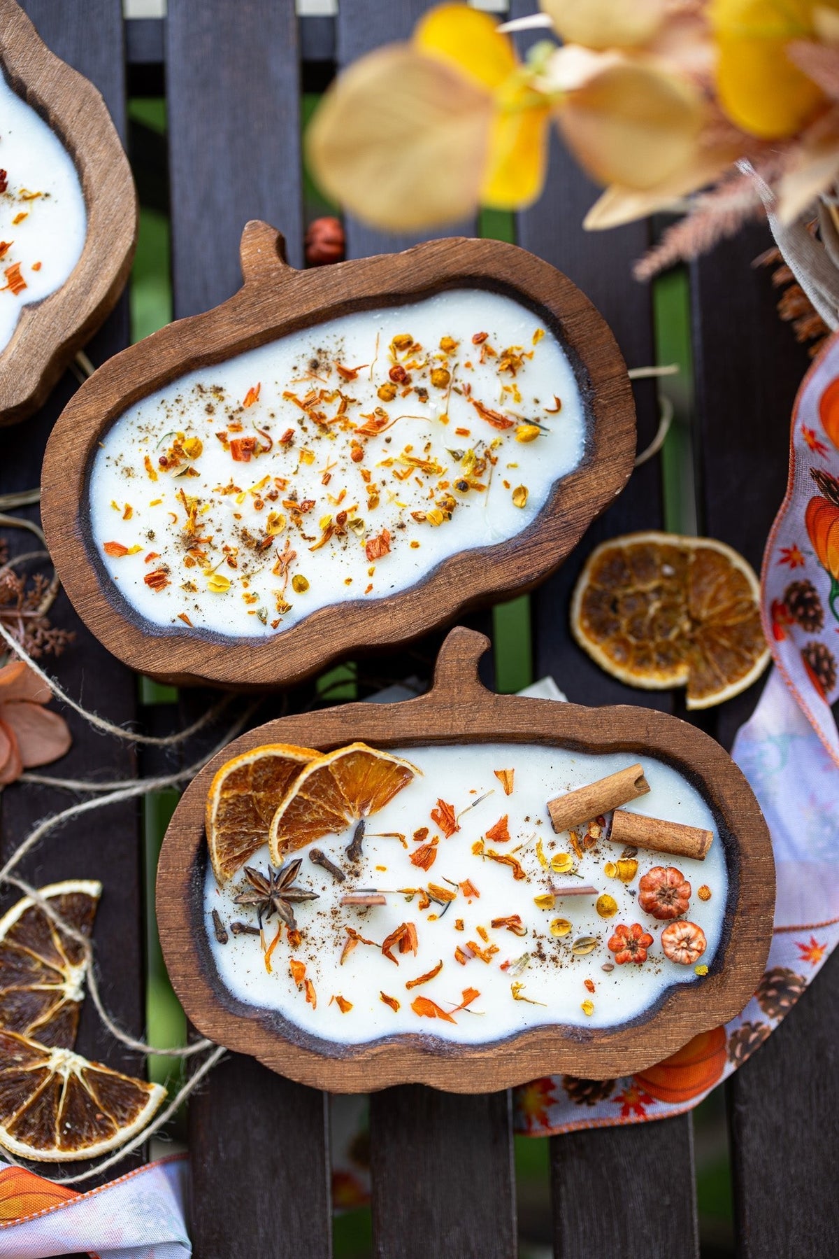 Decorative wooden bowls with white substance, orange slices, and cinnamon sticks on a dark surface.