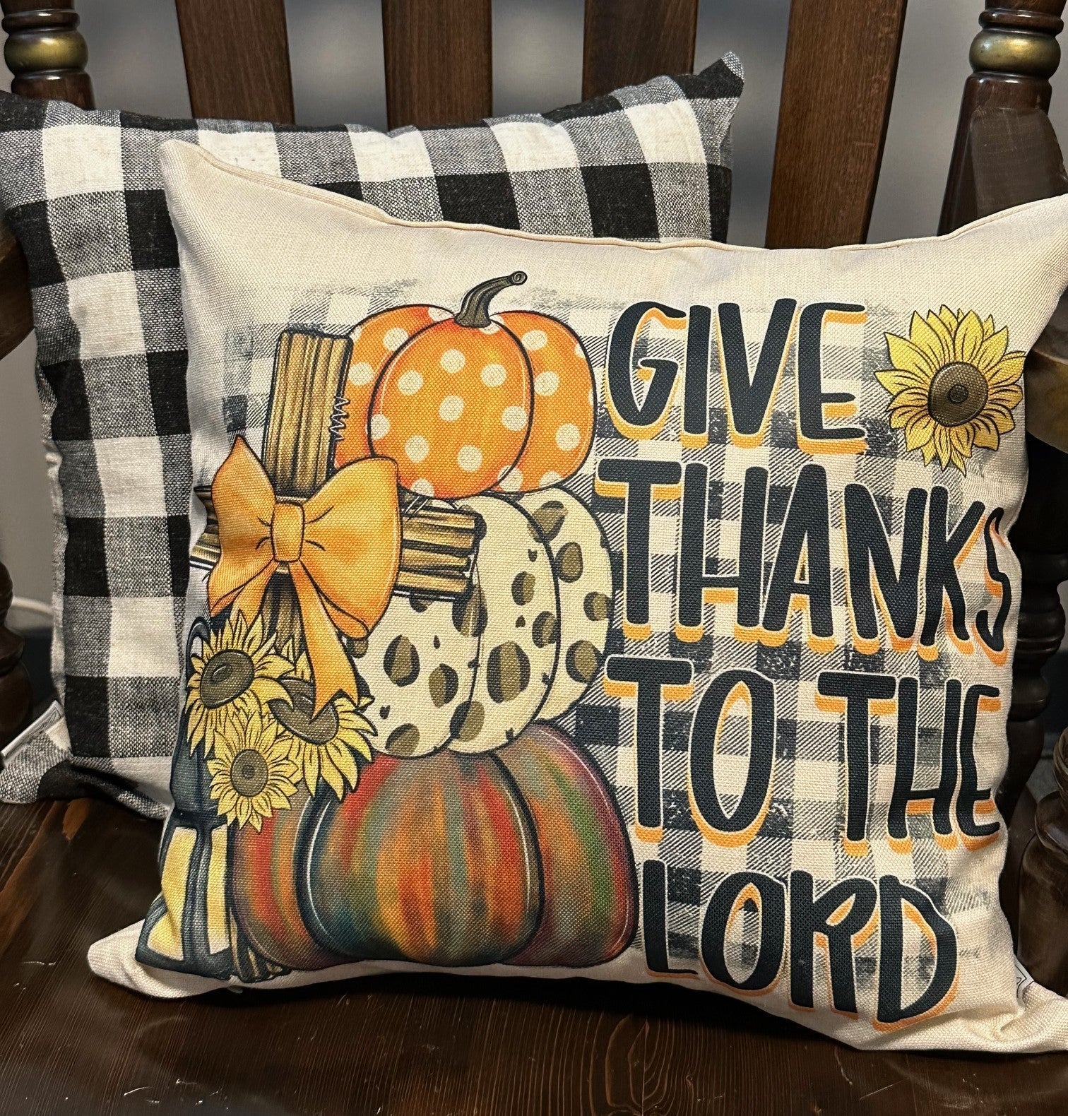 Decorative pillow with pumpkins, sunflowers, and 'Give Thanks to the Lord' text on a wooden surface.