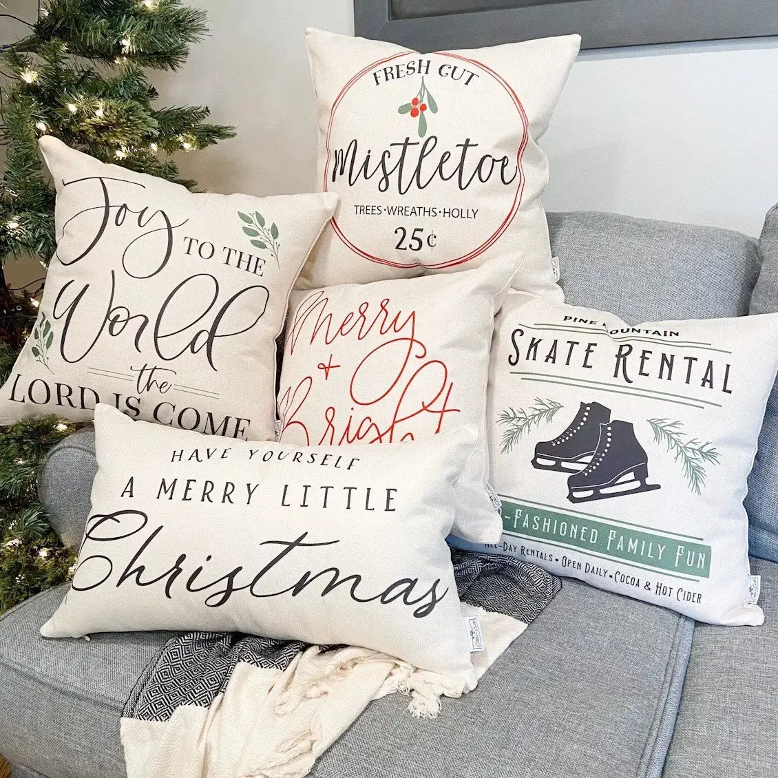 Decorative Christmas pillows on a gray couch with a Christmas tree in the background.