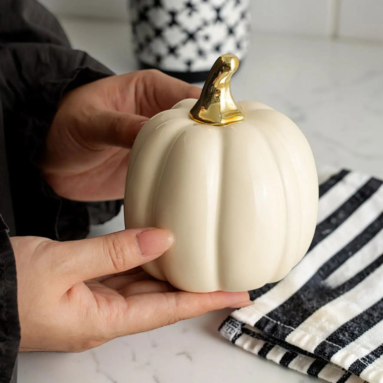 Person holding a small white pumpkin with a gold stem on a marble surface.