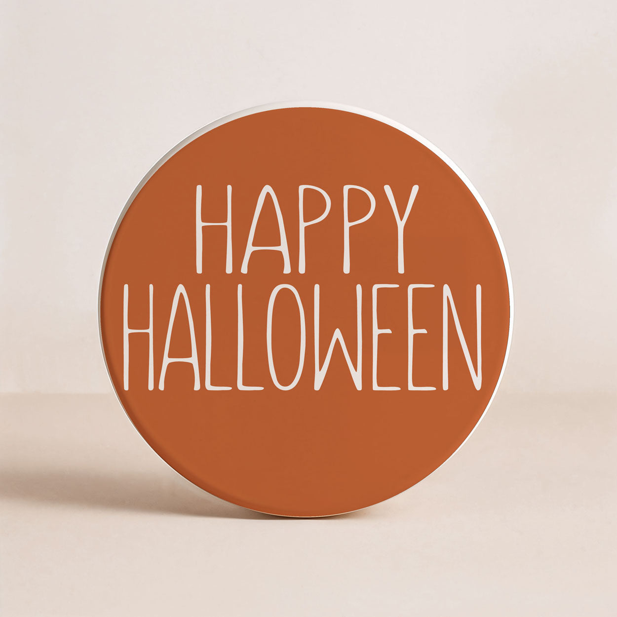 Round brown coaster with 'Happy Halloween' text on a beige background