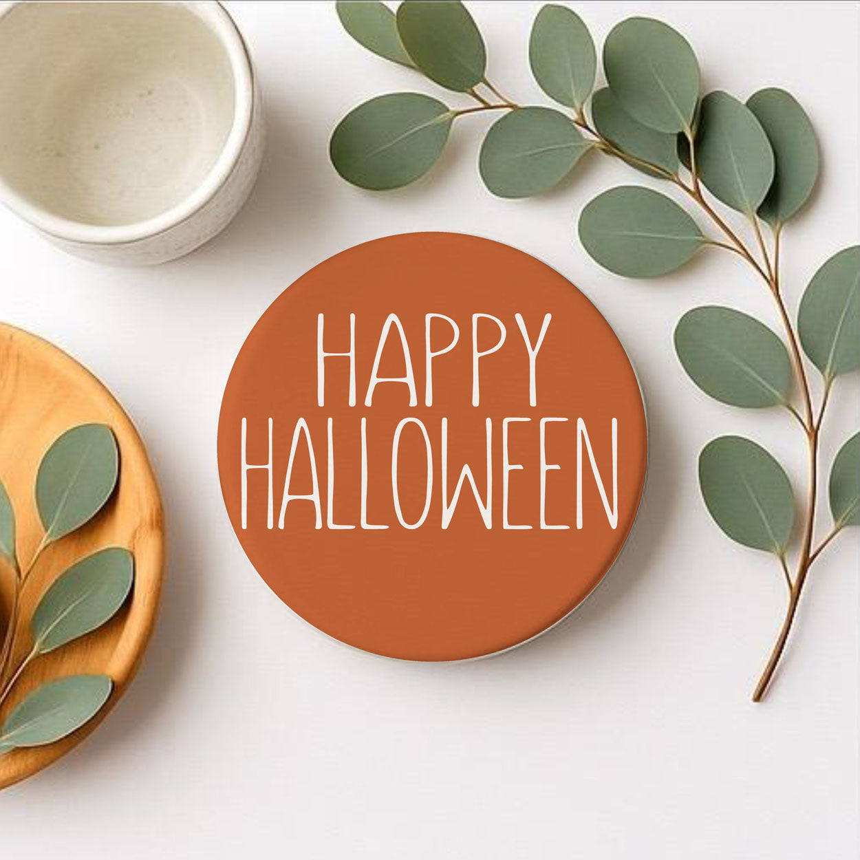 Round orange coaster with 'Happy Halloween' text on a white surface with green leaves.