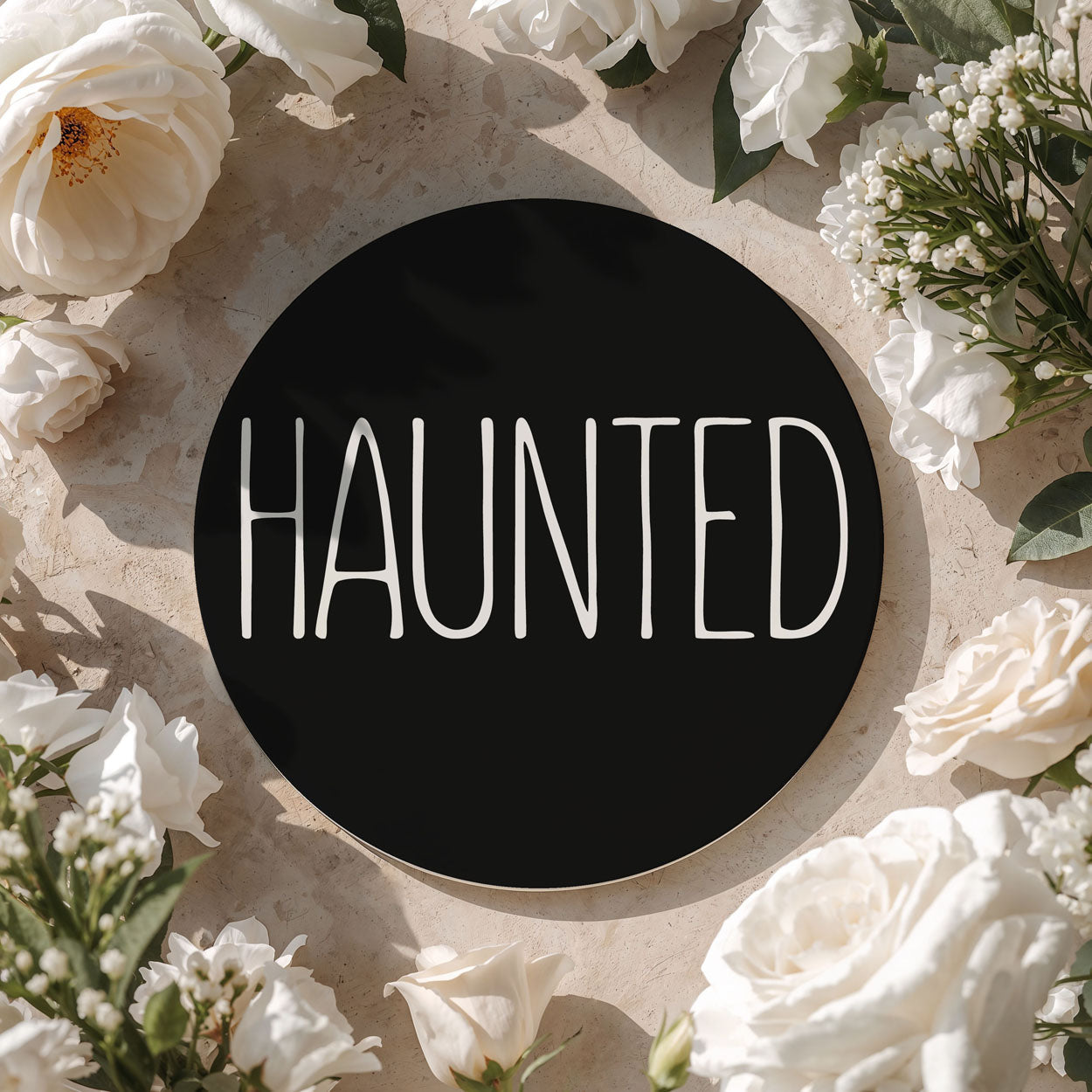Floral arrangement with a black circle in the center displaying the word 'HAUNTED'.
