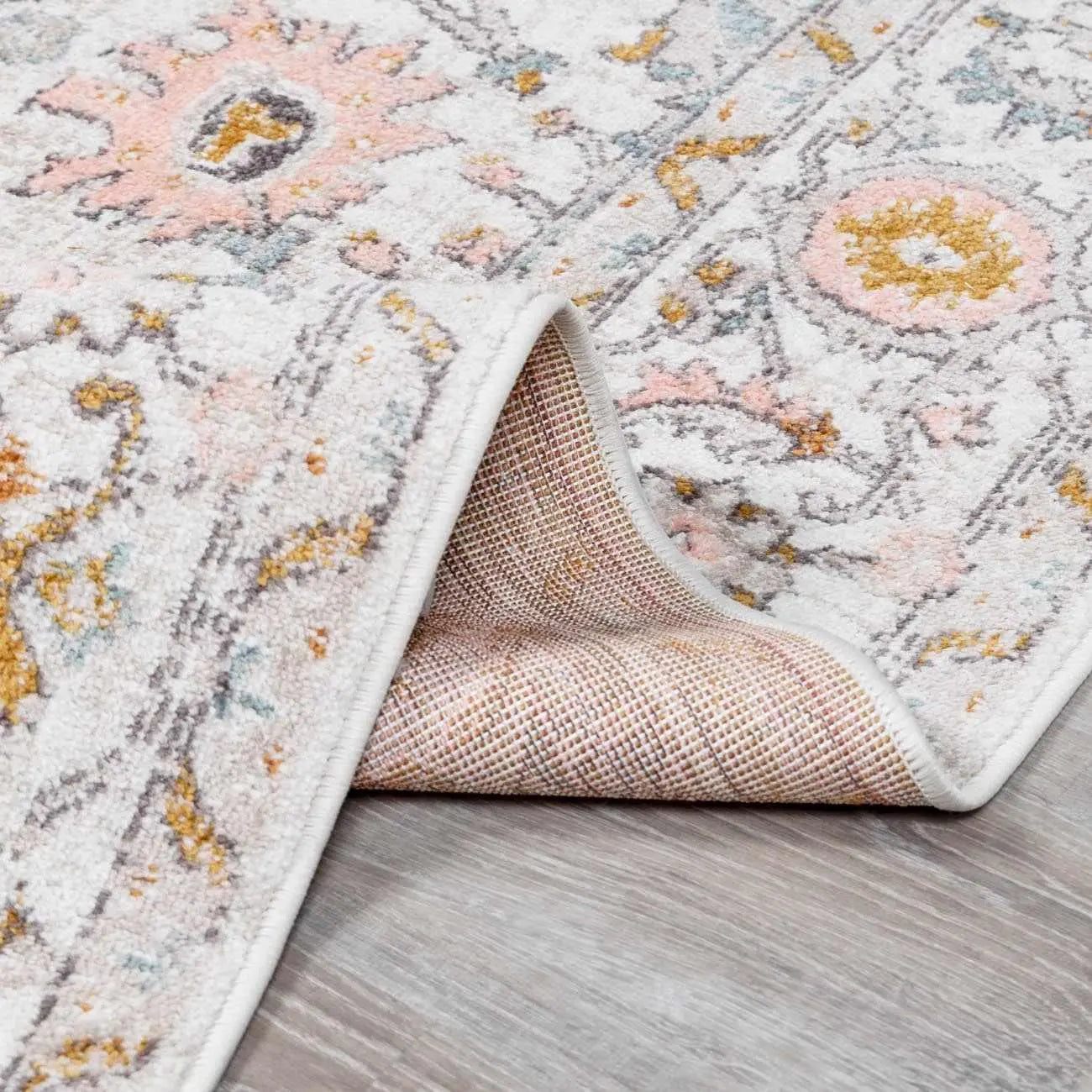 Cozy farmhouse area rug with vintage floral pattern in soft pink, gold, and gray on wood floor
