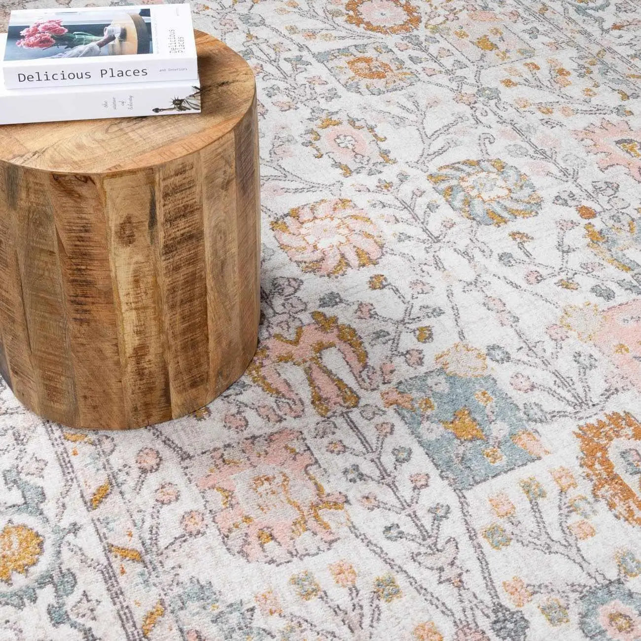 Floral patterned area rug with pastel hues, styled with rustic wood side table and decor books for cozy farmhouse living spaces.