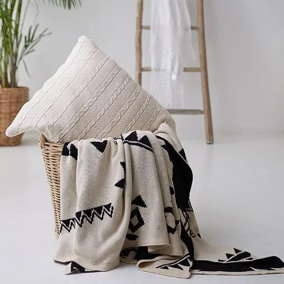 Cozy farmhouse throw blanket with geometric patterns and cable knit pillow in wicker basket