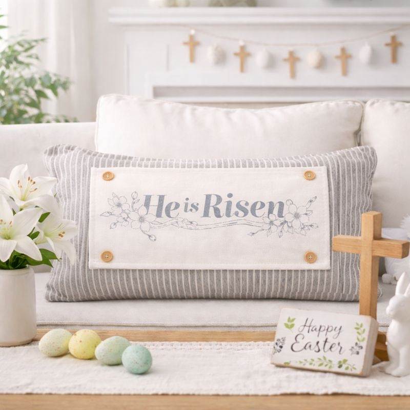 Decorative pillow with 'He is Risen' text on a couch with Easter decorations.