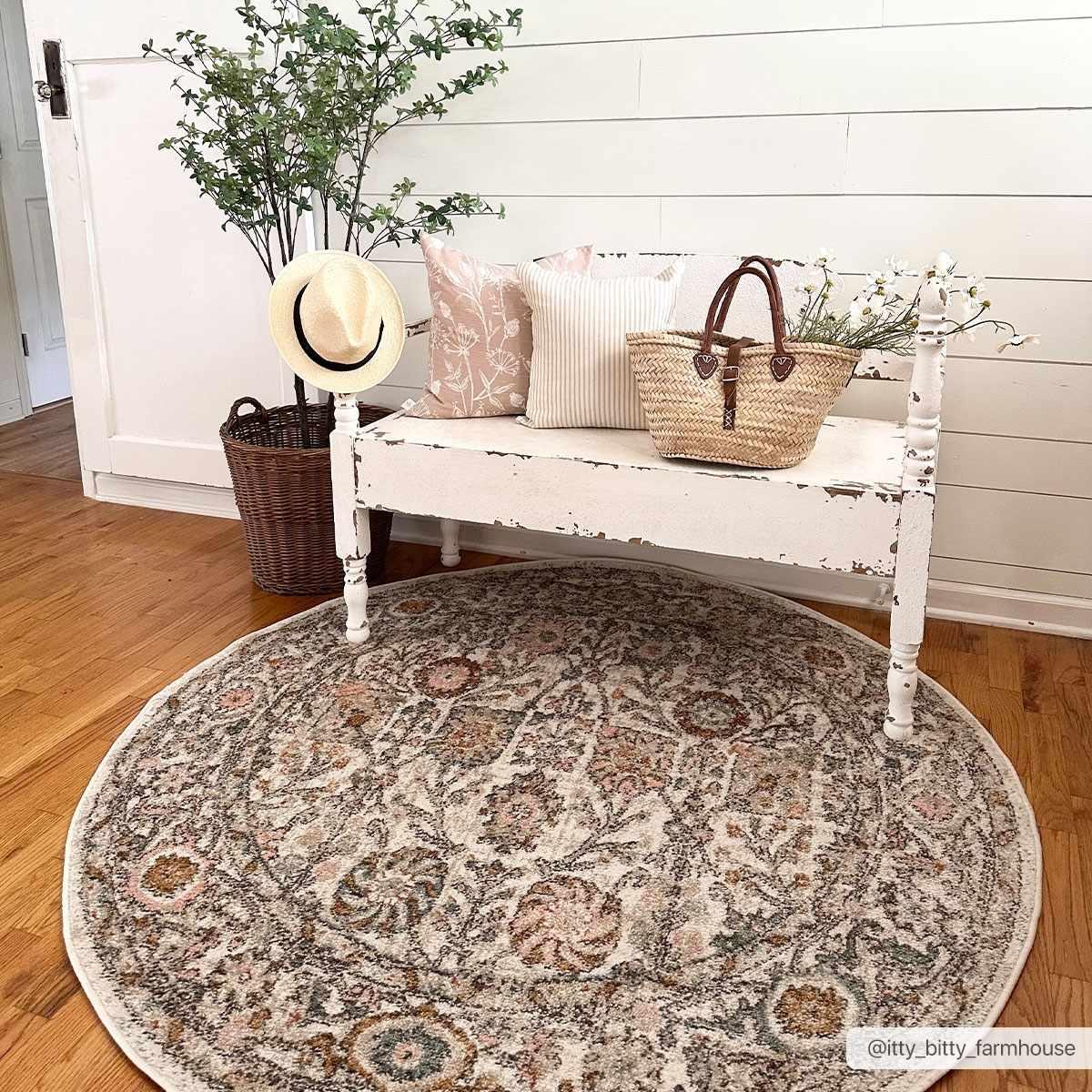 Round floral rug under shabby chic bench with pillows, straw hat, and woven basket in cozy farmhouse entryway