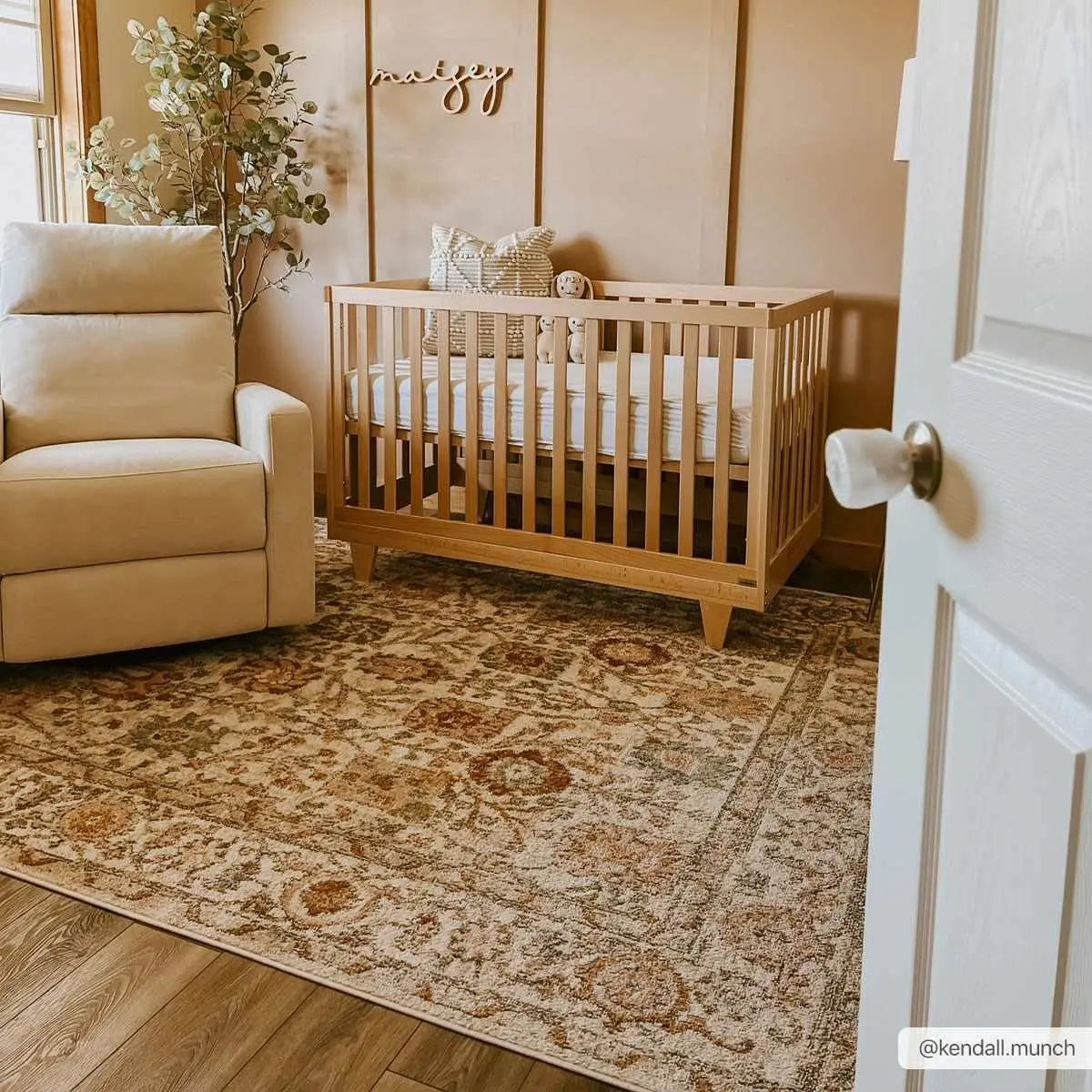 Cozy nursery with wooden crib, floral rug, and beige armchair for peaceful baby room decor