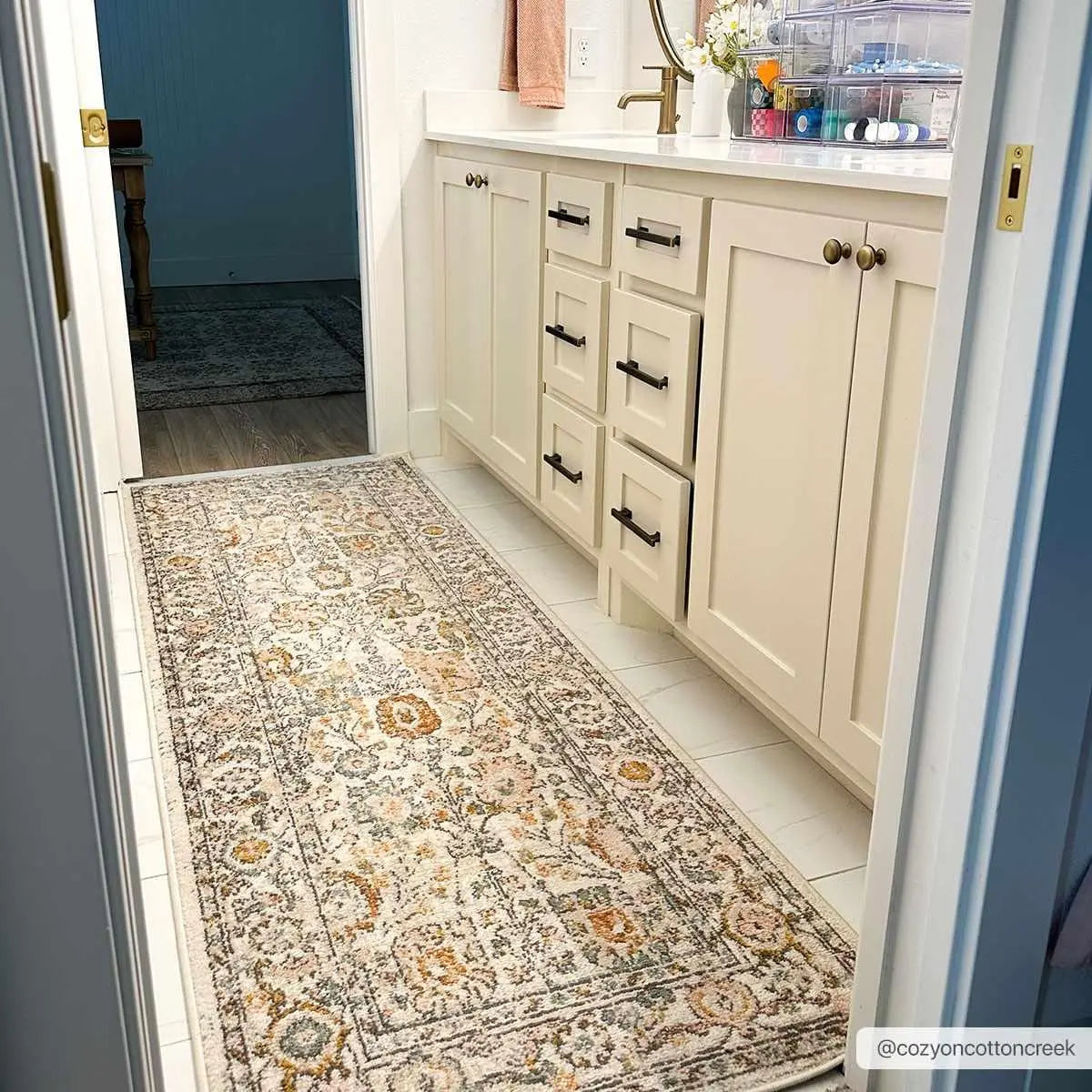 Cozy farmhouse bathroom with vintage floral runner rug, cream vanity, and gold hardware