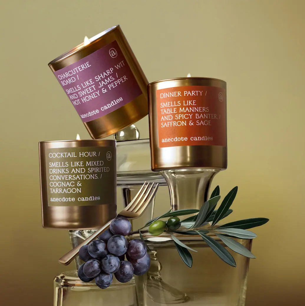 Three candles with labels on a decorative stand with olives and a fork against a beige background
