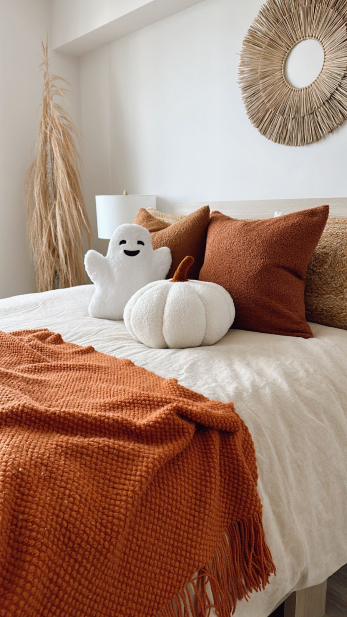 Cozy bedroom with a bed featuring orange pillows and a white plush ghost, with a decorative wall hanging.