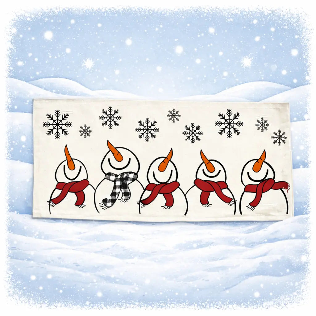 A rectangular cream-colored fabric napkin or tea towel featuring a winter illustration of five snowmen holding red scarves under black snowflakes, set against a snowy blue background with a white border.