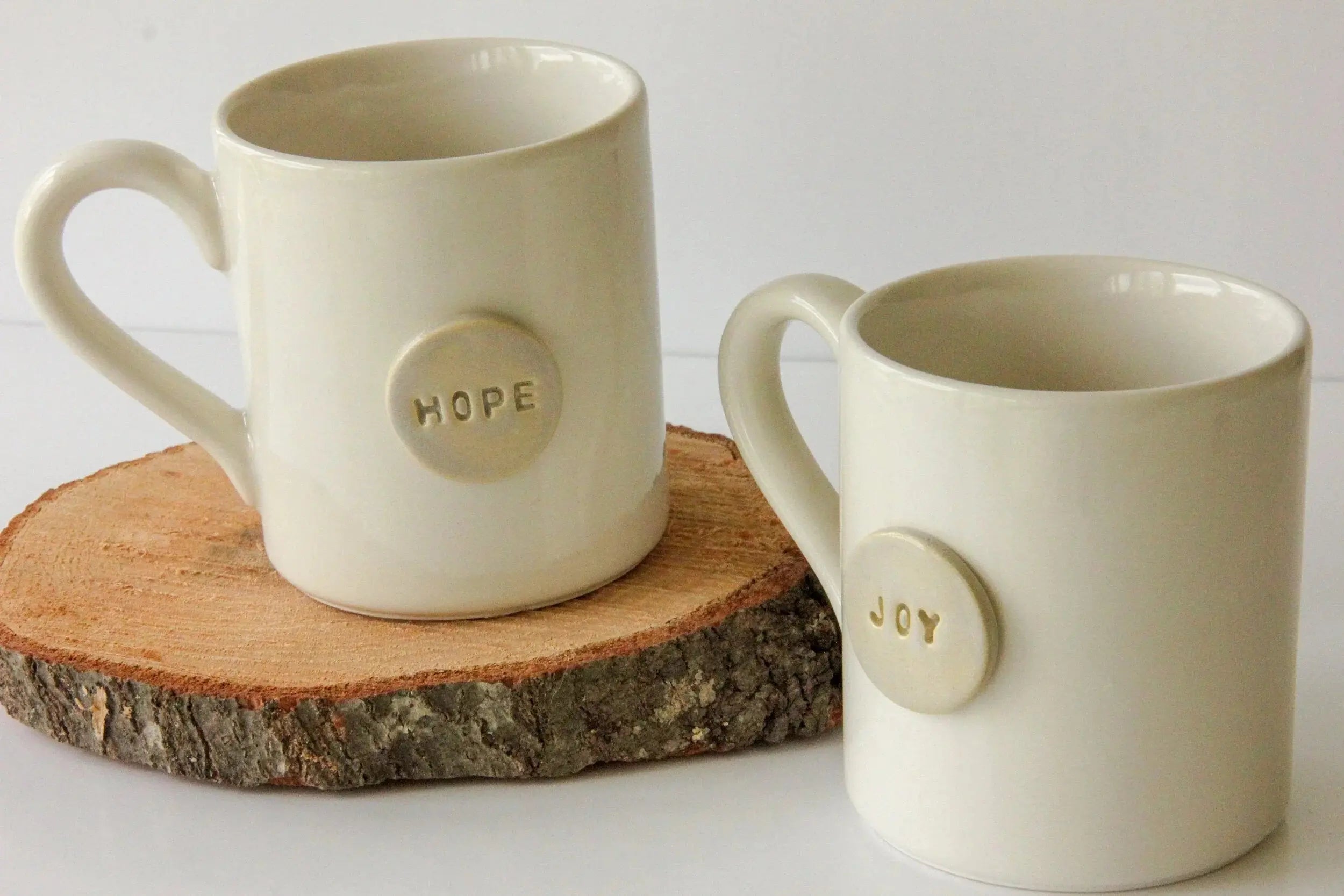 Cream ceramic mugs with 'Hope' and 'Joy' embossed, rustic wood slice display, farmhouse home decor