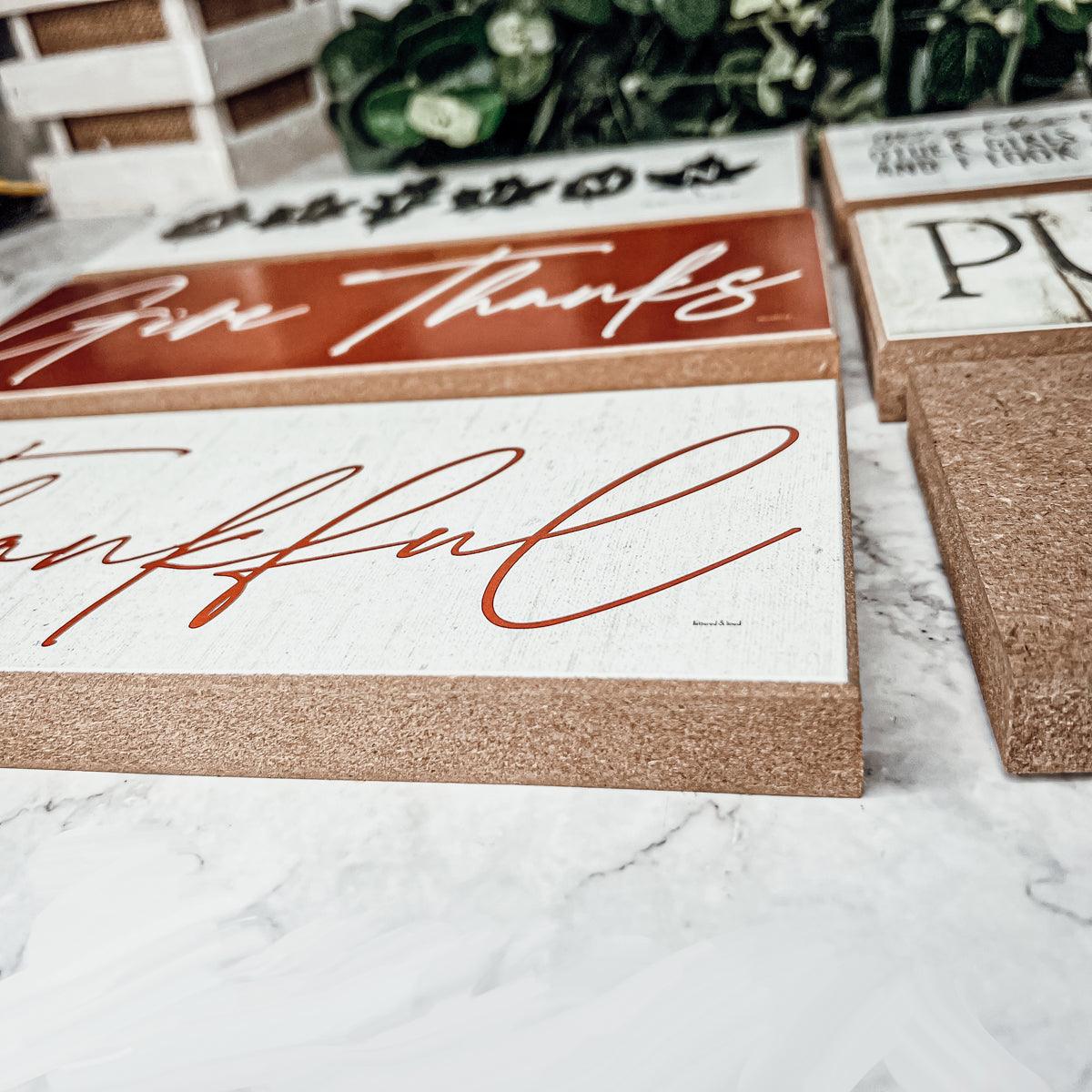 Decorative signs with 'Give Thanks' and 'Grateful' text on a marble surface.