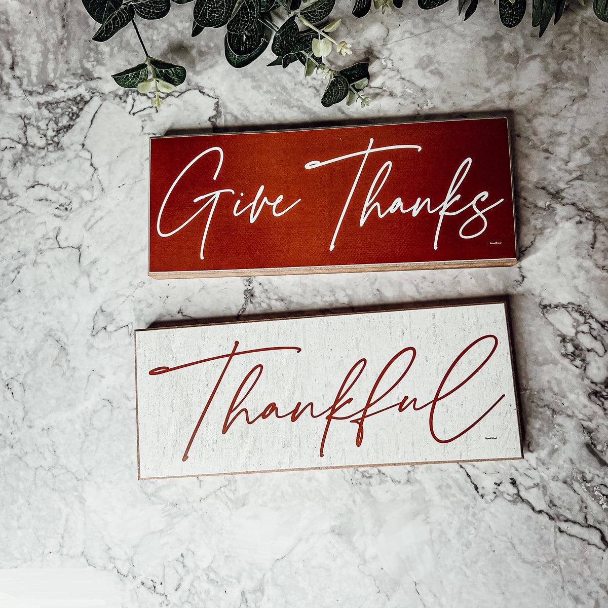 Two wooden signs with 'Give Thanks' and 'Thankful' text on a marble surface.