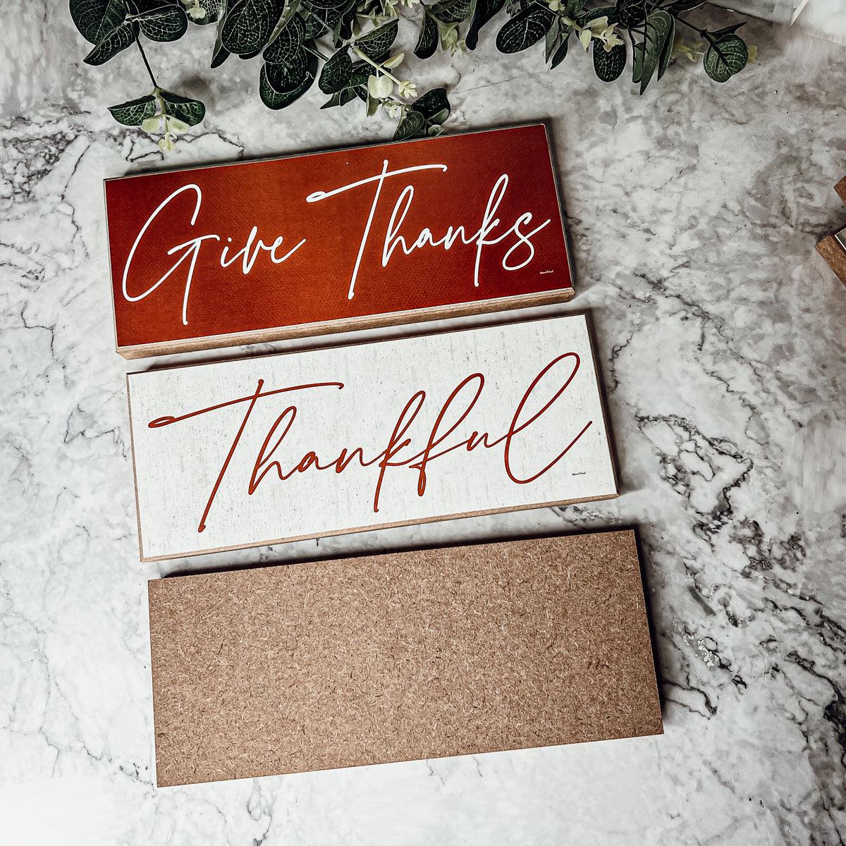 Three wooden signs with 'Give Thanks' and 'Thankful' text on a marble surface.