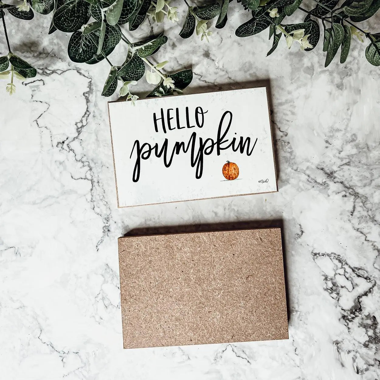 Card with 'Hello Pumpkin' text and a small pumpkin illustration on a marble surface with greenery.