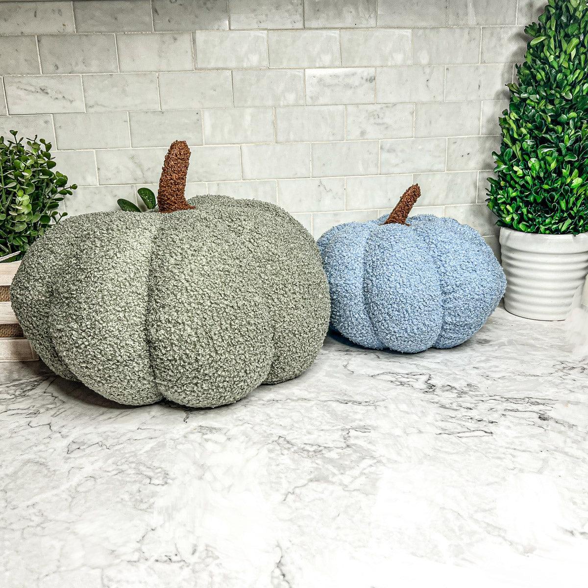Two textured pumpkins, one green and one blue, on a marble surface with a tiled wall background.