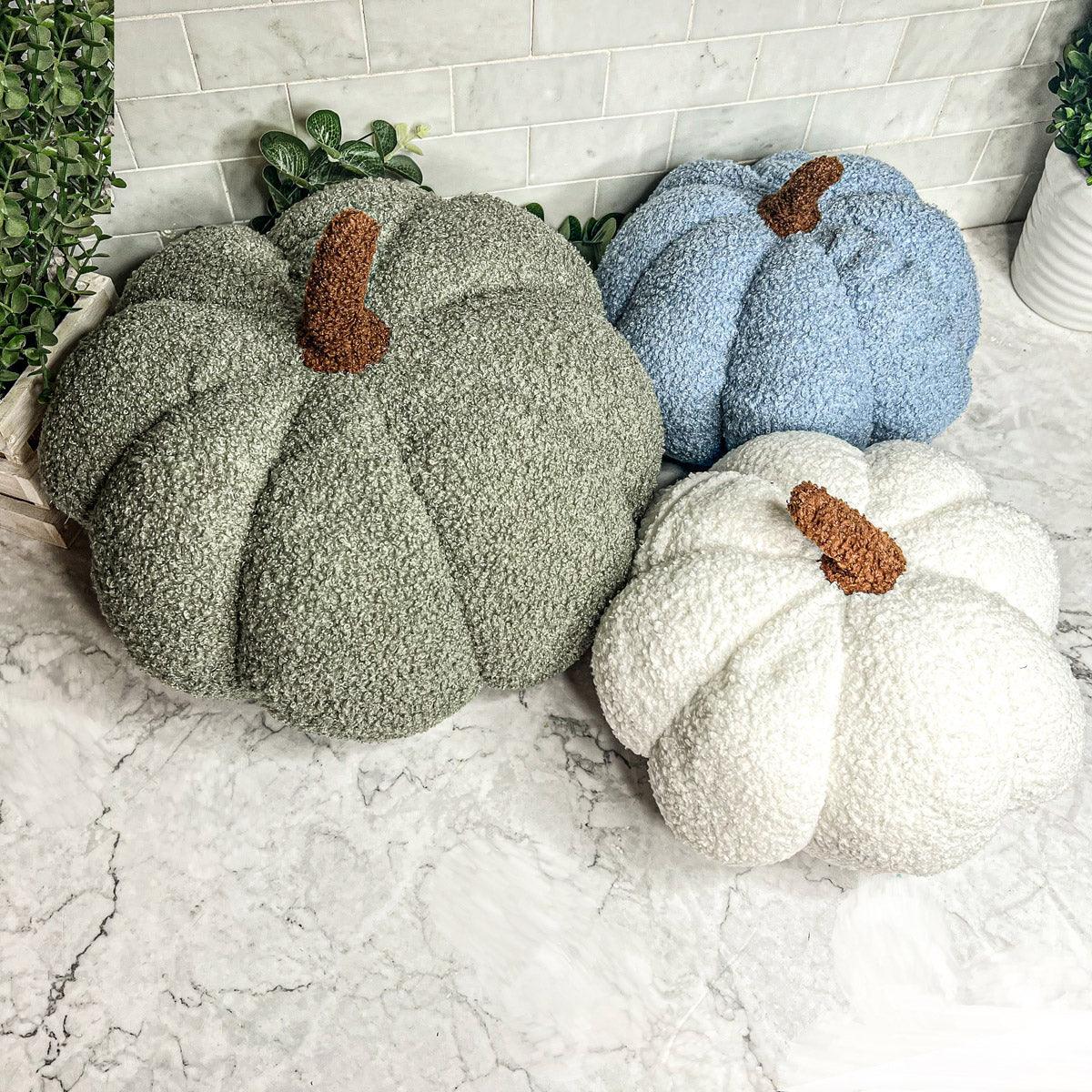 Three textured pumpkins in green, blue, and white on a marble surface with a tiled wall background.
