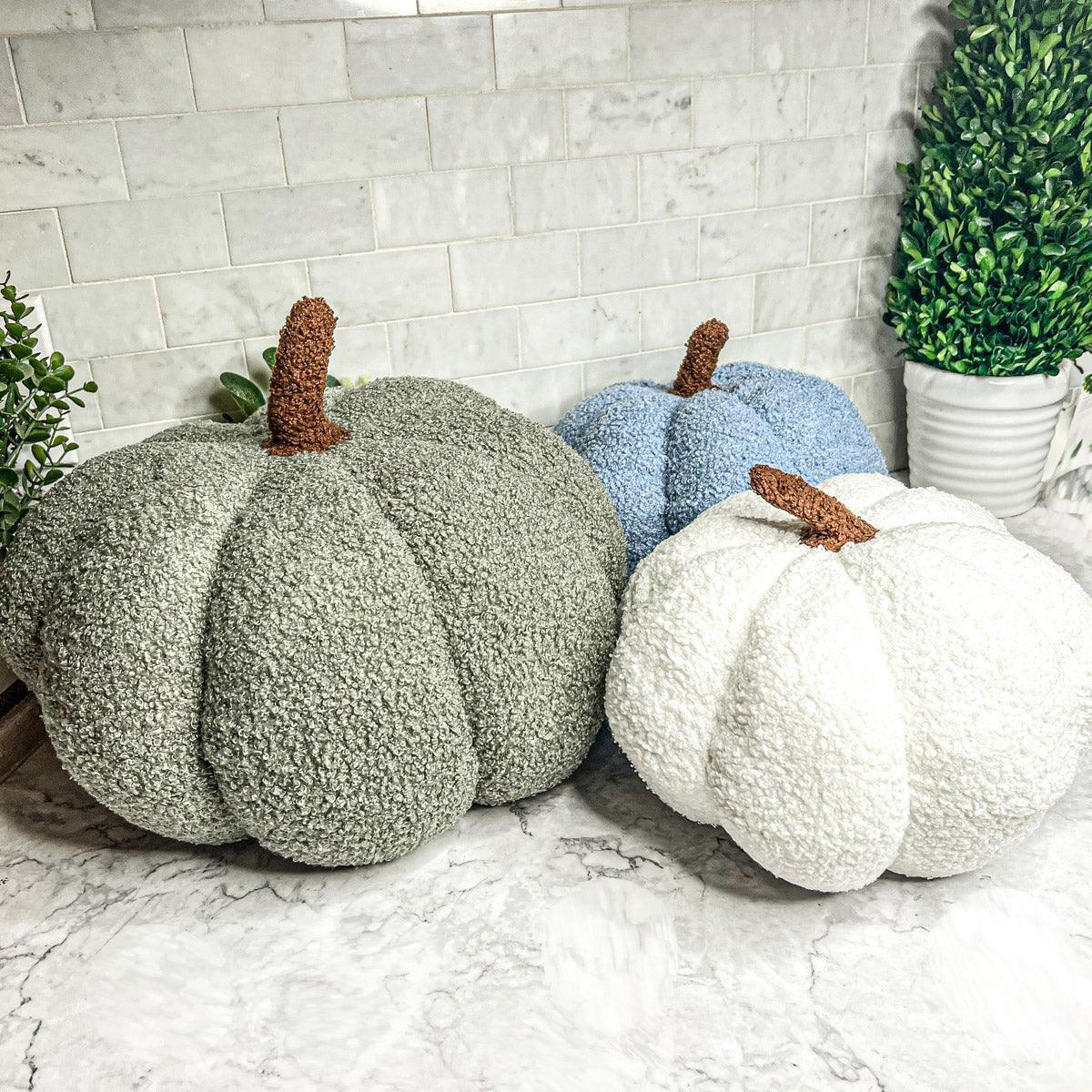 Three textured pumpkins in green, blue, and white on a marble surface with a tiled wall background.