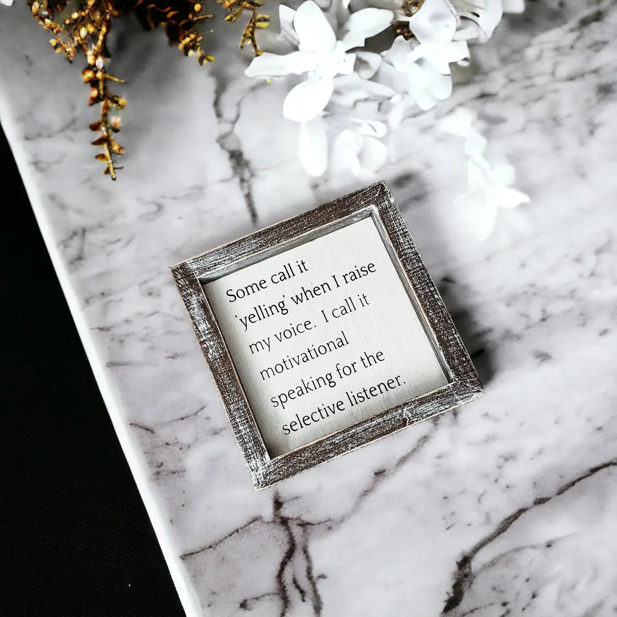 Decorative box with a motivational quote on a marble surface with flowers.