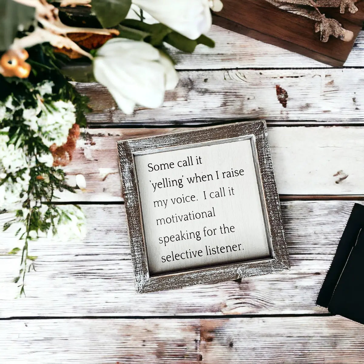 Decorative sign with a quote on a wooden surface with flowers and a book.
