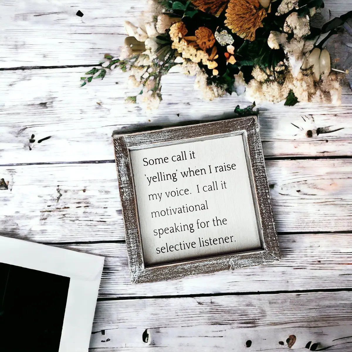 Framed quote on a wooden surface with flowers in the background