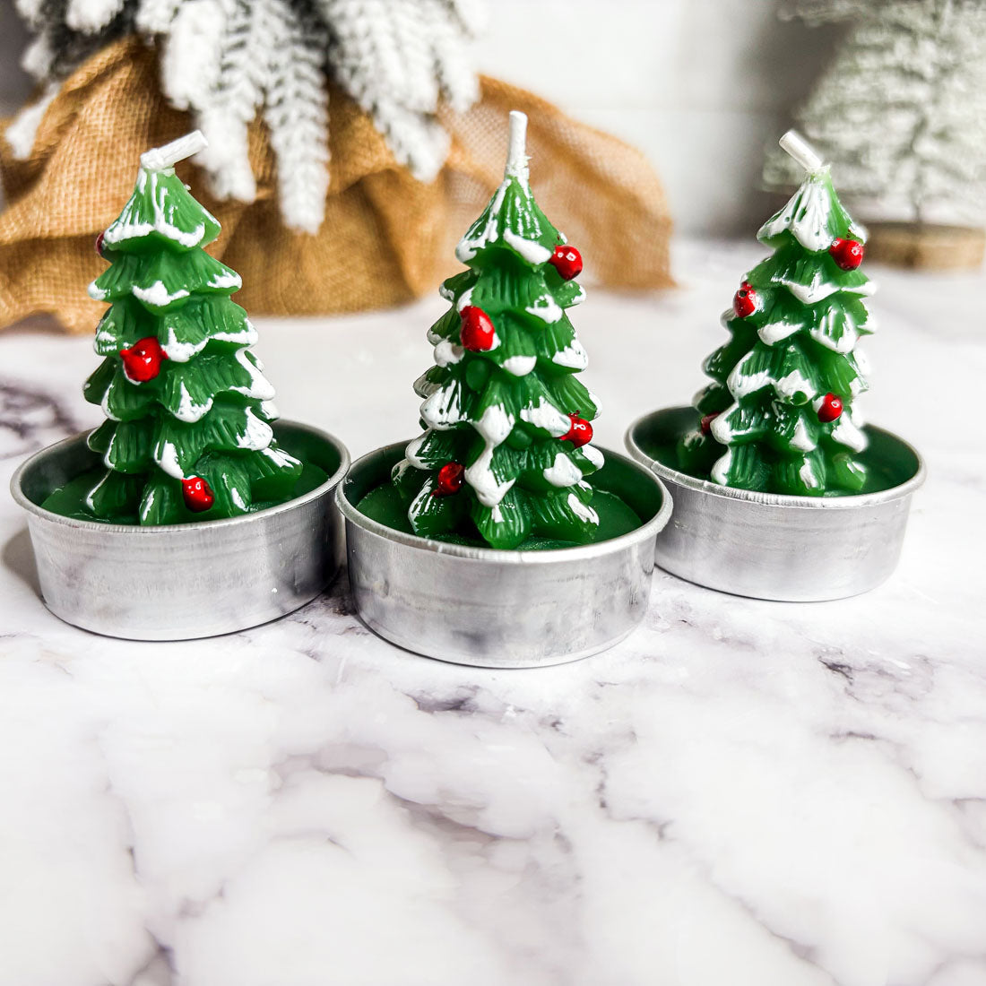 Three Christmas tree-shaped candles in metal holders on a marble surface.