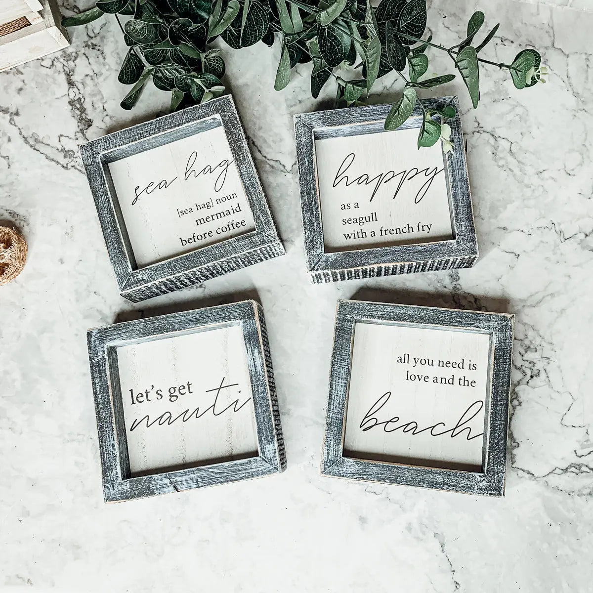 Four framed sayings on a marble surface with greenery above.