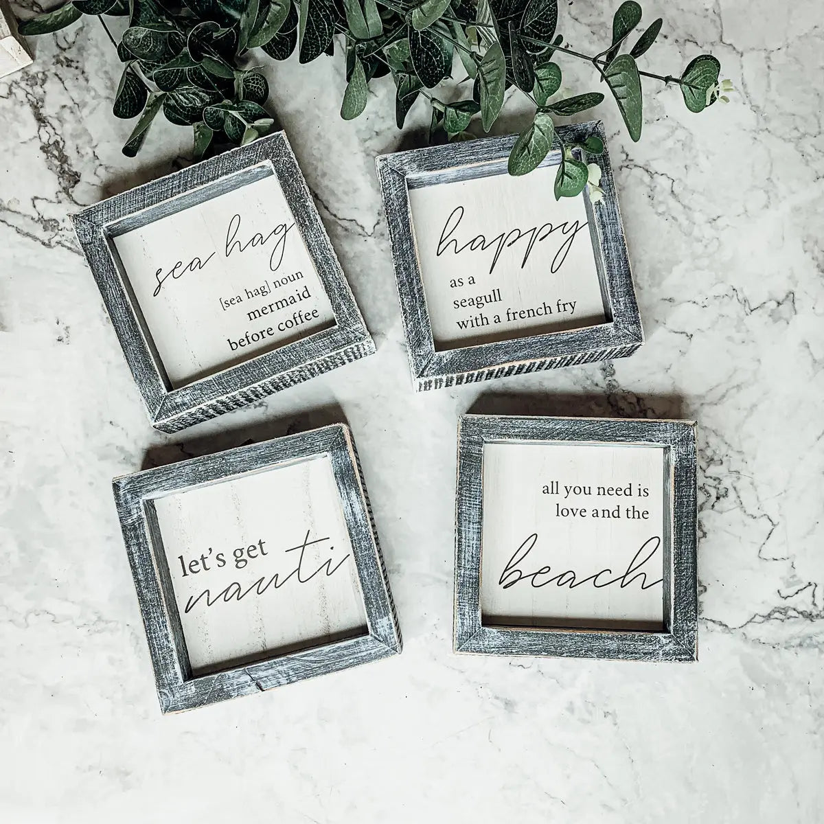 Four framed quotes on a marble surface with greenery.