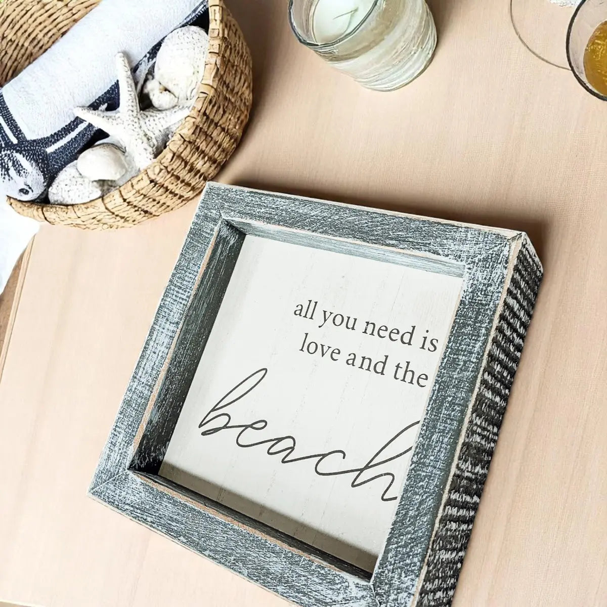 Decorative sign with 'all you need is love and the beach' text on a table with a basket of seashells.